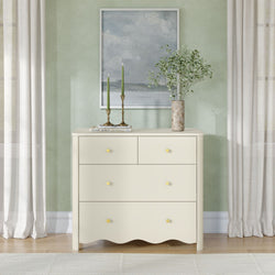 Cream dresser styled for modern coastal entryway decor with framed seascape on a sage green wall, brass candle holders with green taper candles, and a marble vase of baby's-breath beside sheer curtains
