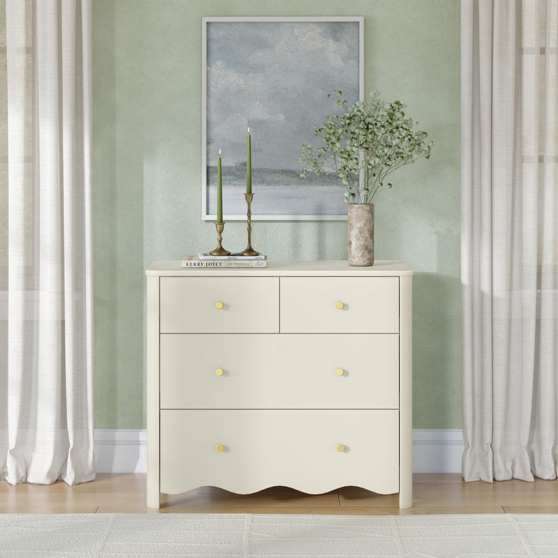 Cream dresser styled for modern coastal entryway decor with framed seascape on a sage green wall, brass candle holders with green taper candles, and a marble vase of baby's-breath beside sheer curtains