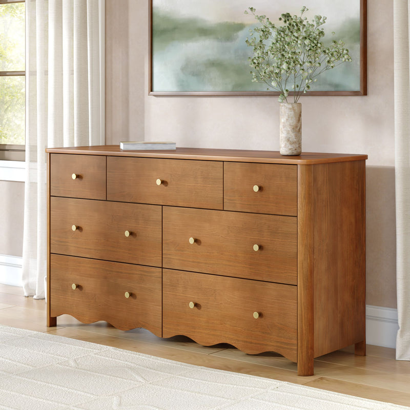 Solid wood dresser with brass knobs, marble vase of green branches and abstract green wall art in a sunlit neutral bedroom with sheer curtains