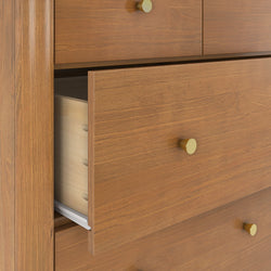 Close-up of oak dresser drawer with brass knob, visible dovetail joinery, wood grain texture and metal drawer slide, partially open modern wooden bedroom furniture