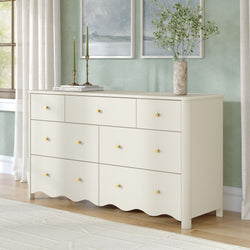 Cream bedroom dresser with gold knobs, green taper candles and marble vase of greenery against a mint wall with coastal framed art