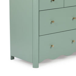 Close-up of mint green wooden dresser corner with three drawers, brass cone knobs, scalloped base and matte finish — modern bedroom storage piece