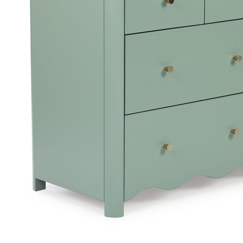 Close-up of mint green wooden dresser corner with three drawers, brass cone knobs, scalloped base and matte finish — modern bedroom storage piece