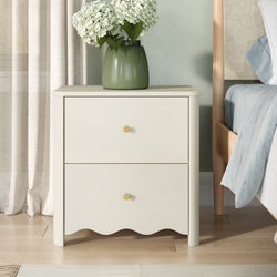 Cream three-drawer nightstand with gold knobs and green ceramic vase of white hydrangeas next to light-wood bed in modern bedroom