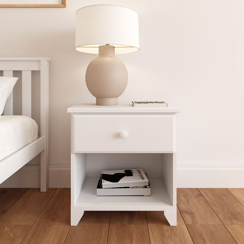 White nightstand with drawer and shelf featuring a modern table lamp and books, in a minimalist bedroom setting.