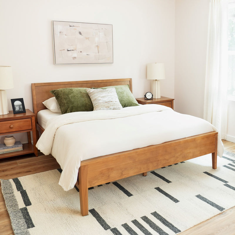 Modern minimalist bedroom with wooden bed frame, cream bedding, green velvet pillows, matching nightstands, table lamps, abstract wall art and geometric area rug