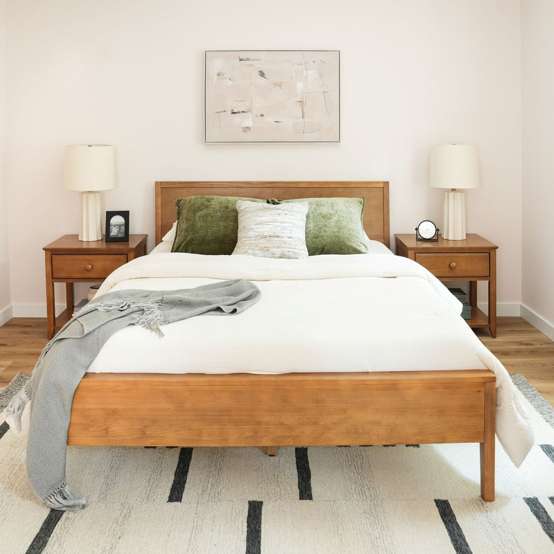 Minimalist modern bedroom with wooden bed frame, layered white bedding, green velvet pillows, matching wood nightstands, ceramic lamps and abstract wall art