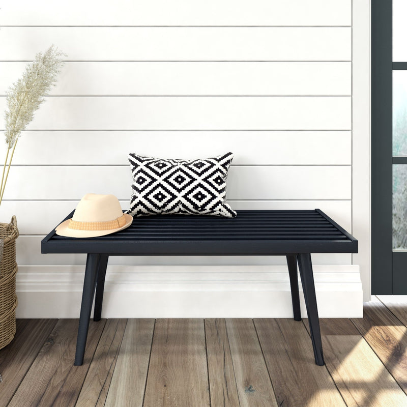 Modern black bench with patterned cushion and straw hat in a stylish home interior with wooden flooring and white shiplap wall.