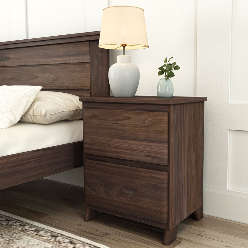 Dark wood nightstand with lamp and plant, positioned next to bed with white pillow, set in modern bedroom.