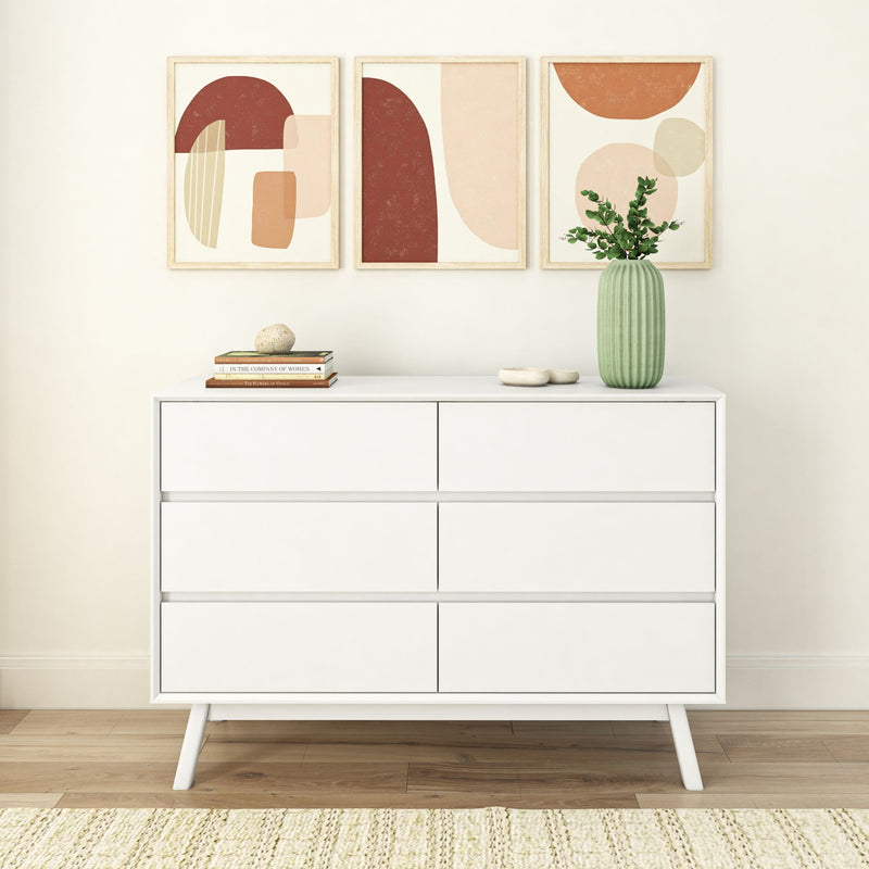 Modern white dresser with six drawers in a minimalist room featuring abstract wall art and a decorative green vase.