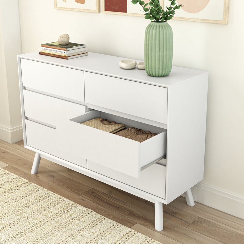 Modern white dresser with open drawer showcasing neatly folded clothes, decorative green vase, and minimalistic decor in a stylish living space.