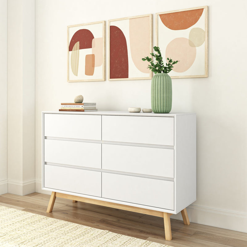 Mid-century modern white dresser with six drawers, wooden legs, and a plant vase, framed by abstract wall art in a minimalist living room.