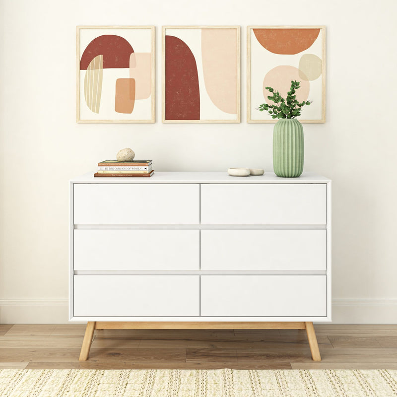 Mid-century modern white dresser with six drawers, wooden legs, green vase, books, and abstract art decor on a beige wall.