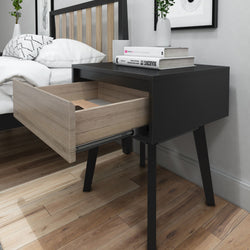 Modern black nightstand with open wooden drawer next to bed in stylish bedroom.