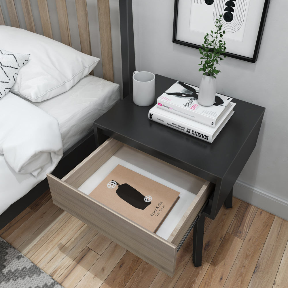 Modern bedroom nightstand with open drawer, books, a white mug, and a small plant in a vase.