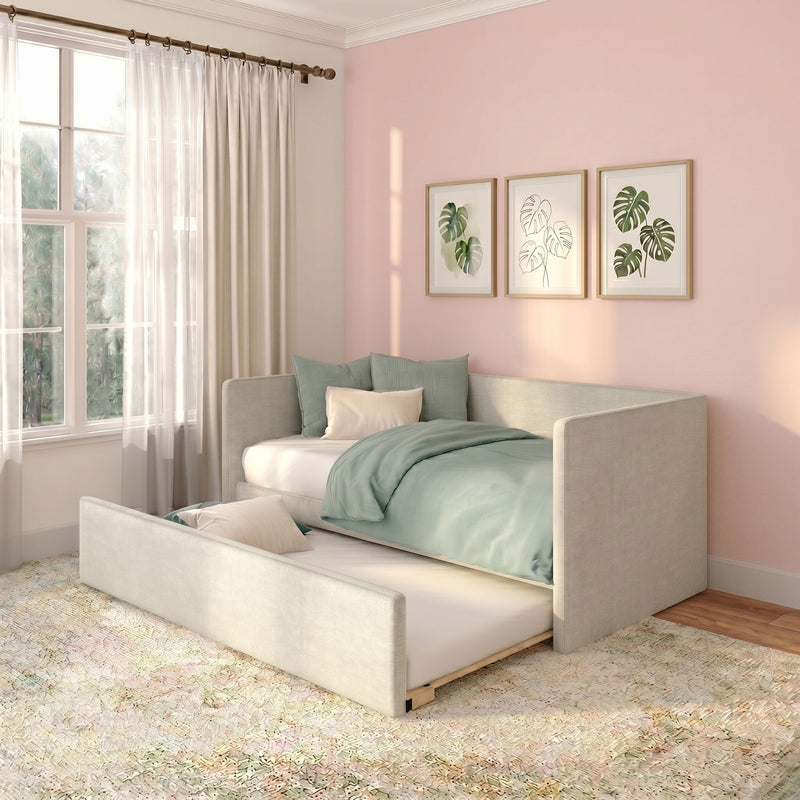 Pastel pink bedroom with upholstered daybed and pull-out trundle, mint-green bedding, sheer curtains, and framed monstera botanical prints in soft natural light.