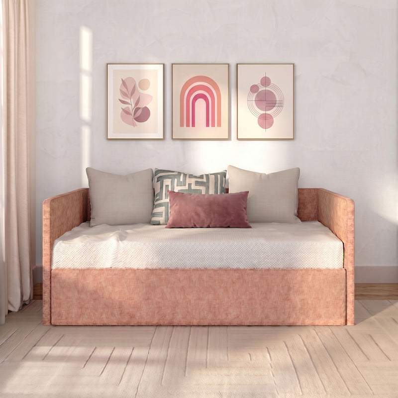 Modern boho living room daybed with blush-pink velvet pillow, geometric throw cushion, and three framed pink abstract art prints on a neutral wall in soft natural light