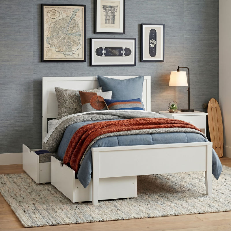 Modern bedroom with white platform bed and under-bed storage drawers, blue quilt and rust knit throw, decorative pillows, framed gallery wall, bedside lamp and skateboard accent