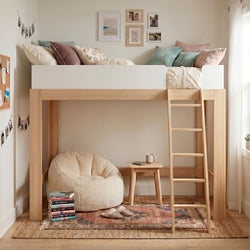 Wooden loft bed with ladder and cozy reading nook with plush bean bag, stacked books, boho pillows, rug and gallery wall