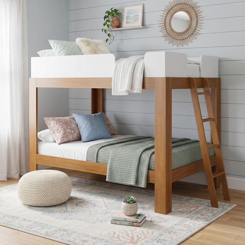 Modern wooden loft bunk bed in kids' room with white guardrails, pastel pillows, green waffle throw, ladder, knitted pouf, coastal rug and rattan sunburst mirror