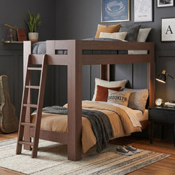 Modern twin-over-twin wooden loft bunk bed with ladder, cozy tan and gray bedding and decorative pillows, Brooklyn accent pillow, bedside lamp, rug and shelf decor in a stylish dark-gray teen bedroom