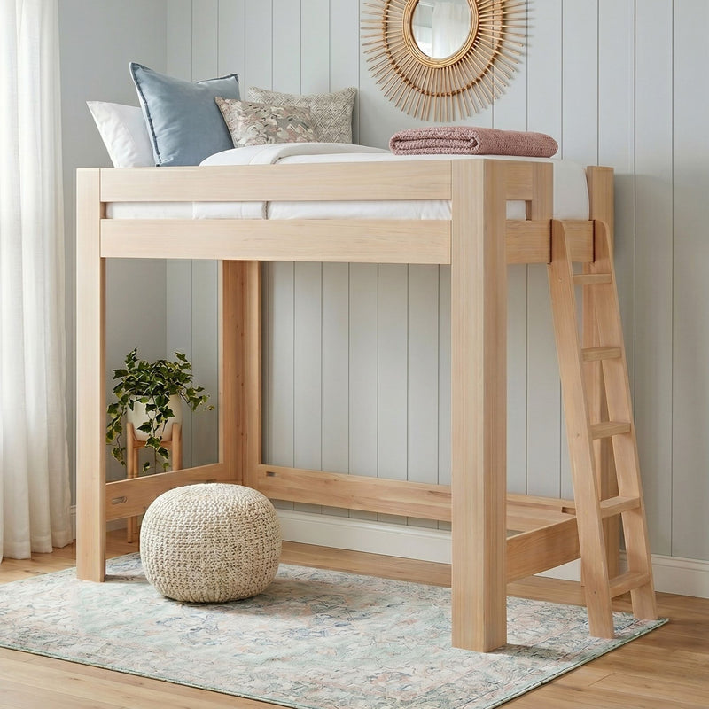 Natural wood loft bed with ladder in a neutral children's bedroom, styled with pastel pillows, rattan sunburst mirror, knitted pouf, potted plant and pastel rug