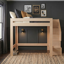 Modern light-wood loft bunk bed with built-in staircase, pillows and rug against a black accent wall with framed art and brass wall sconces